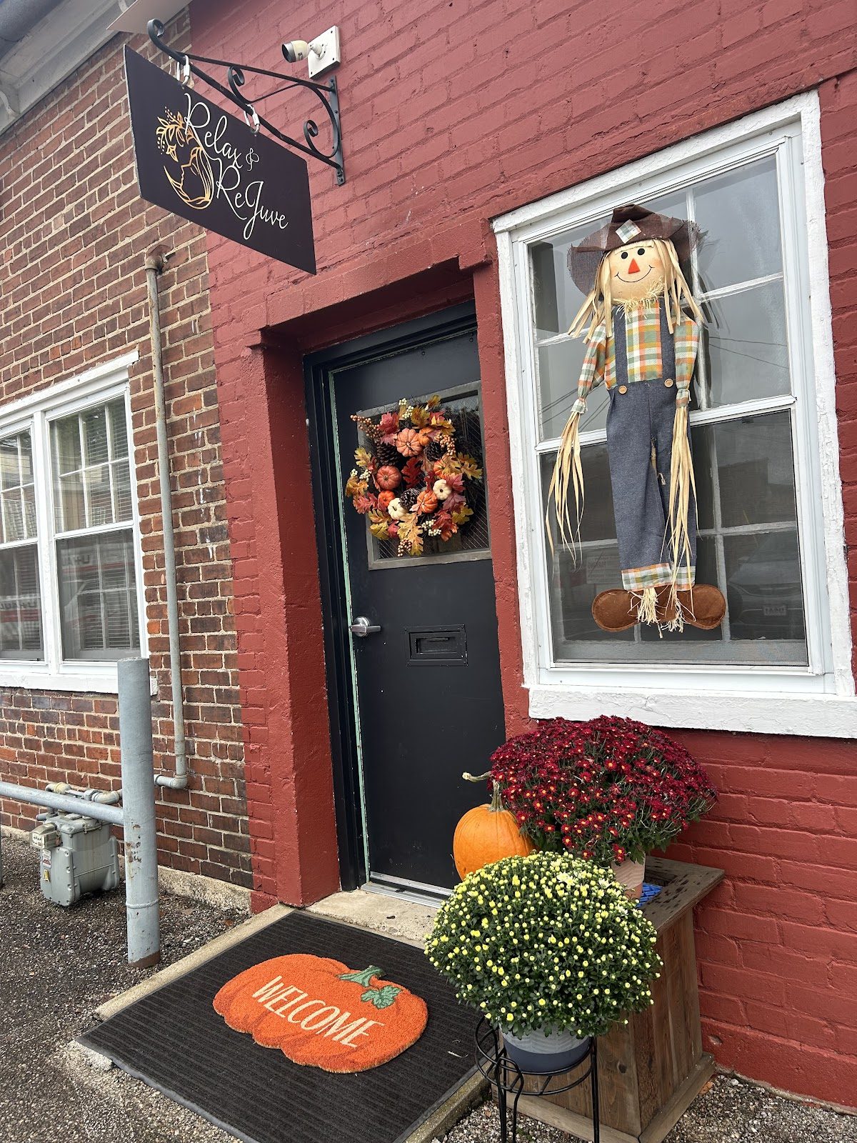 The Relax & ReJuve storefront on East Main Street: red brick, a black hanging sign, fall wreath, mums and pumpkins by the door